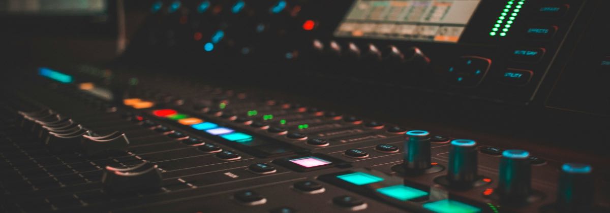 Illuminated audio mixing console with equalizer knobs next to a laptop