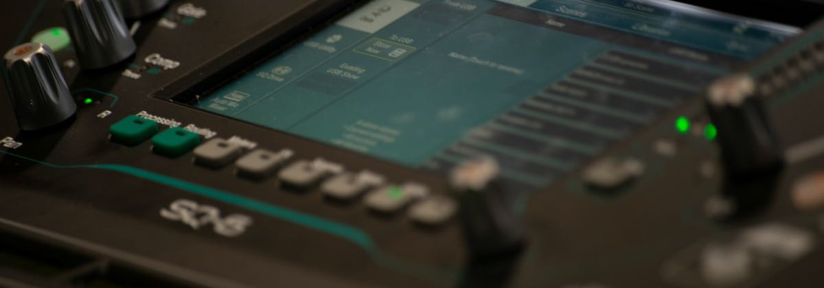 Digital audio mixer in front of a computer monitor and keyboard in a home studio