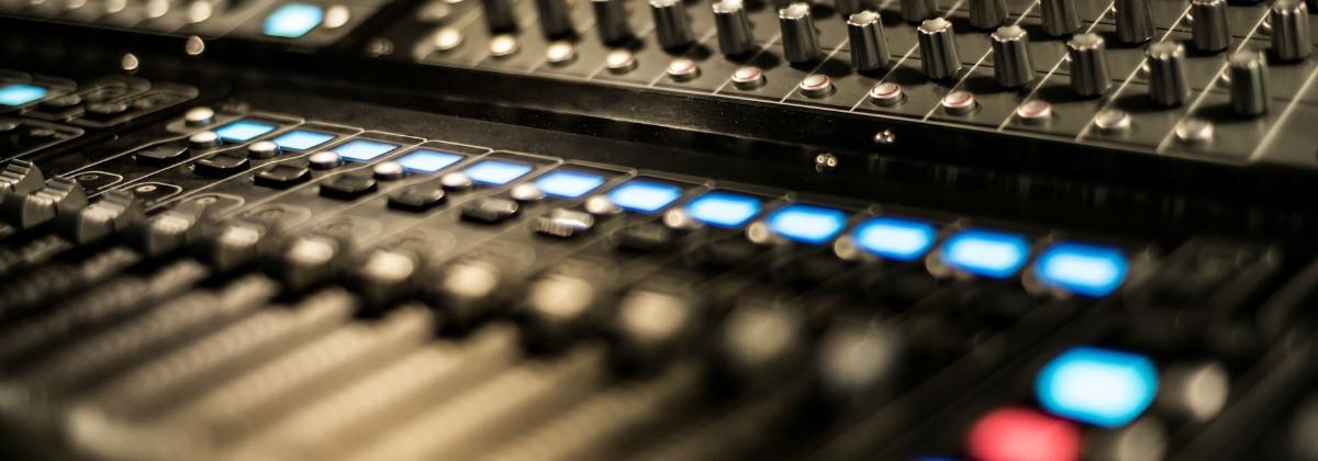 Close-up of a DJ mixer with illuminated faders, knobs and level meters
