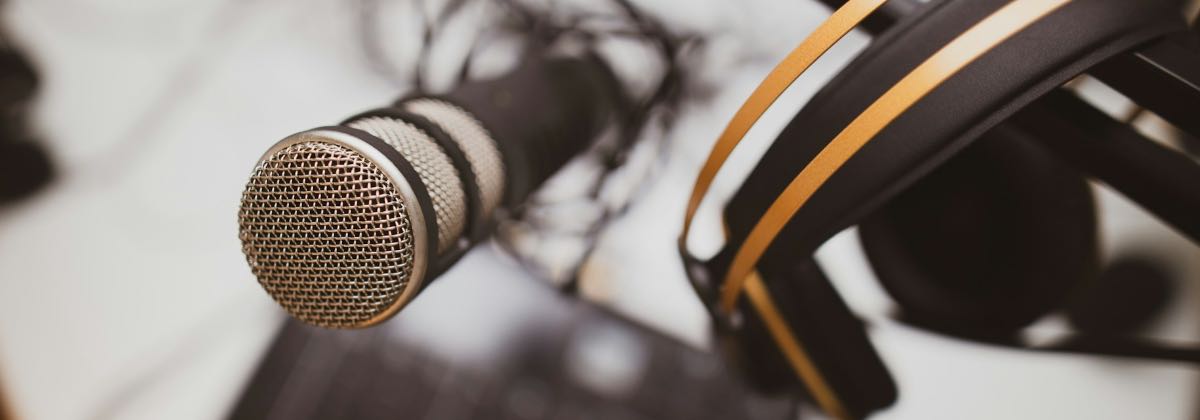 Podcast microphone on a desk next to studio headphones and a small mixing desk