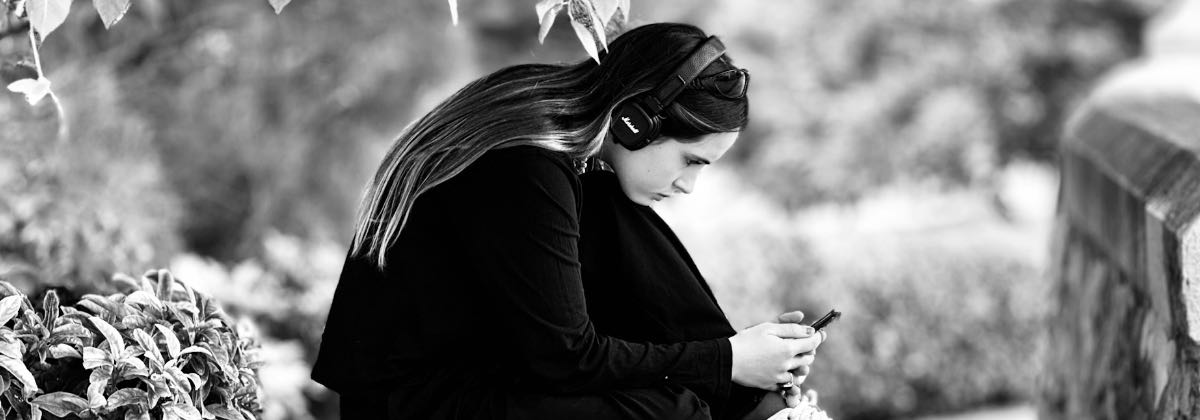 Junge Frau hört draußen mit Kopfhörern einen Slowed-and-Reverb-Song auf ihrem Smartphone